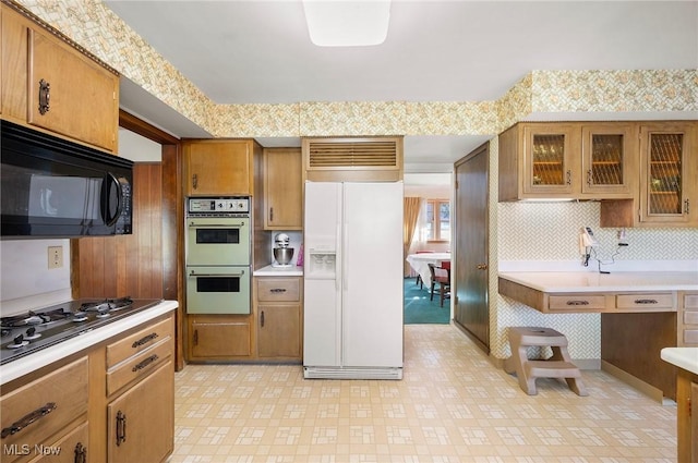 kitchen featuring brown cabinets, wallpapered walls, black appliances, and light countertops