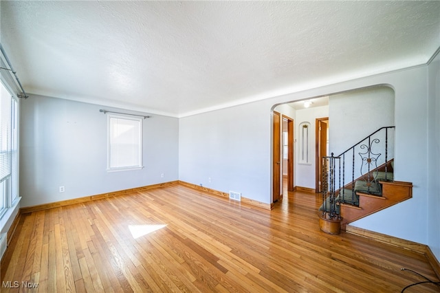 spare room with arched walkways, visible vents, light wood-style flooring, and a textured ceiling