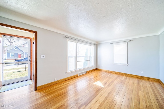 unfurnished living room featuring light wood-style flooring, baseboards, visible vents, and a textured ceiling