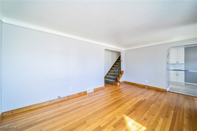 spare room featuring stairway, baseboards, visible vents, and light wood-type flooring