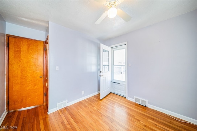 empty room featuring ceiling fan, visible vents, baseboards, and hardwood / wood-style floors