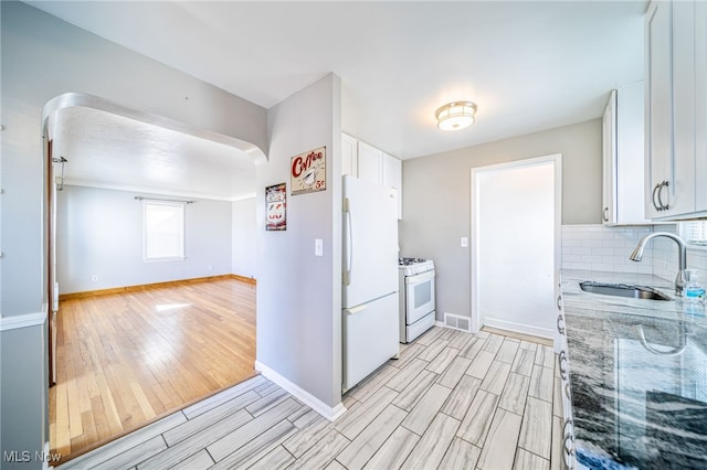 kitchen featuring a sink, white appliances, light wood finished floors, decorative backsplash, and light stone countertops