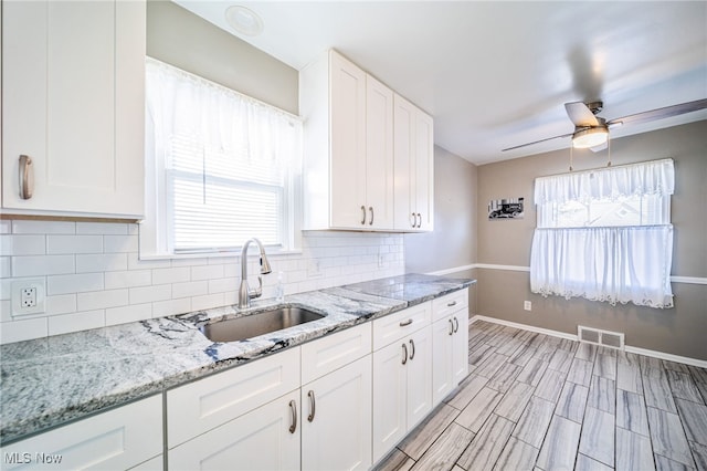 kitchen with visible vents, white cabinetry, decorative backsplash, and a sink