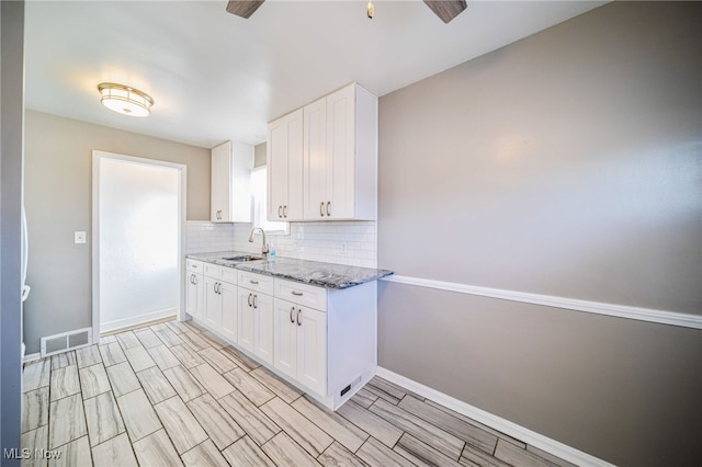 kitchen featuring visible vents, white cabinets, light stone countertops, and a sink