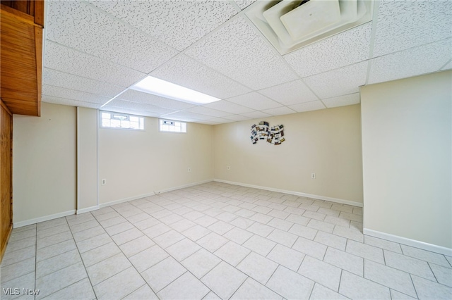 basement with a paneled ceiling and baseboards