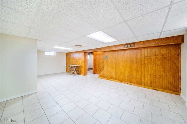 below grade area featuring a drop ceiling, wood walls, a bar, and baseboards