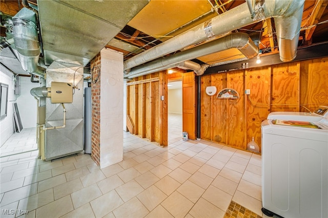 basement featuring water heater, washing machine and dryer, and wood walls