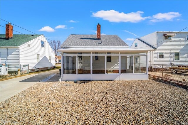 back of house featuring fence, a chimney, a sunroom, and a shingled roof