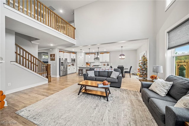 living room with visible vents, light wood-style flooring, stairway, and baseboards