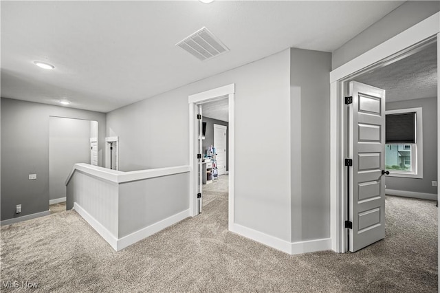 hallway featuring an upstairs landing, baseboards, visible vents, and carpet floors