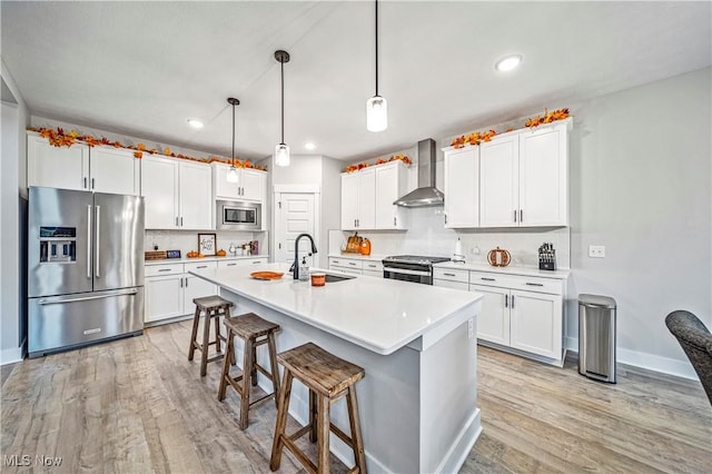 kitchen with a sink, light wood-type flooring, appliances with stainless steel finishes, and wall chimney exhaust hood