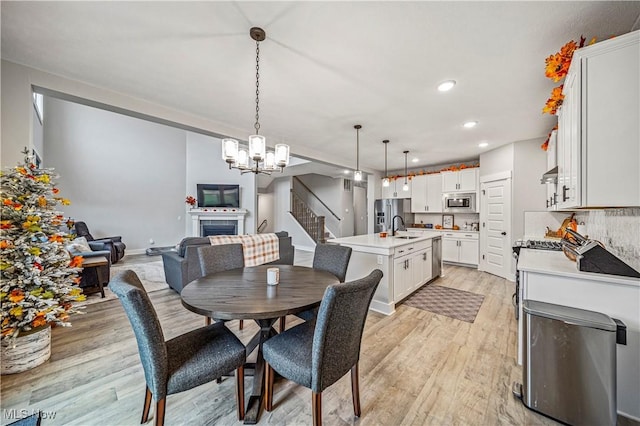 dining area with a notable chandelier, light wood-style flooring, recessed lighting, stairway, and a fireplace