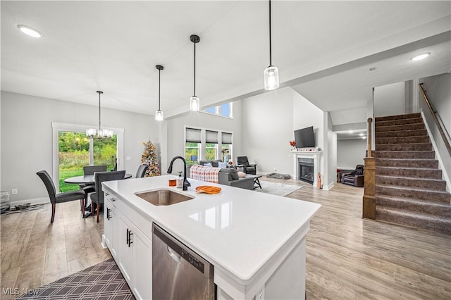 kitchen with a sink, stainless steel dishwasher, white cabinets, a fireplace, and light wood finished floors