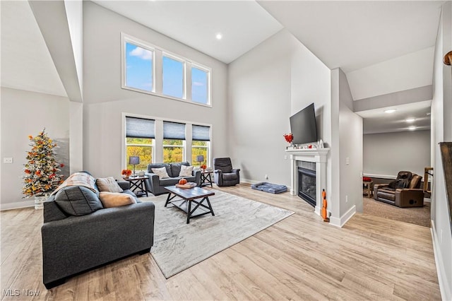 living area with a glass covered fireplace, a towering ceiling, baseboards, and wood finished floors