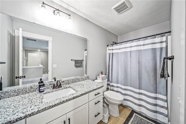 full bathroom featuring visible vents, toilet, a textured ceiling, wood finished floors, and vanity