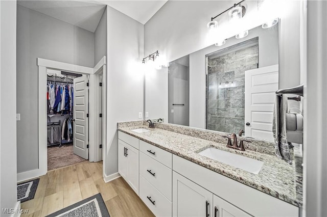 full bathroom with a sink, a walk in closet, wood finished floors, and a tile shower