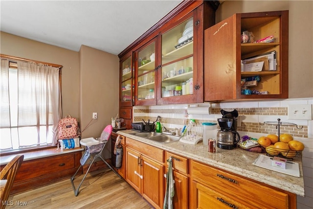 kitchen with backsplash, light wood-style flooring, glass insert cabinets, and a sink