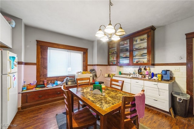 kitchen featuring an inviting chandelier, freestanding refrigerator, hanging light fixtures, dark wood-type flooring, and glass insert cabinets