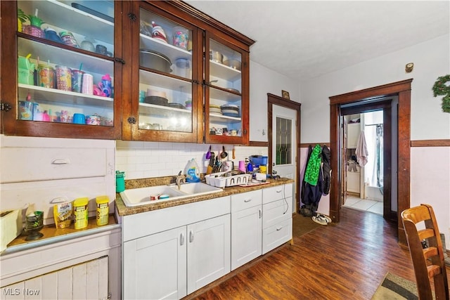 kitchen with a sink, glass insert cabinets, light countertops, white cabinets, and dark wood-style flooring