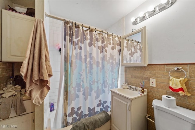 full bath featuring toilet, vanity, wainscoting, shower / tub combo, and tile walls