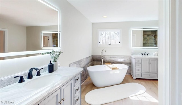 full bath with tile walls, a freestanding bath, two vanities, and a sink