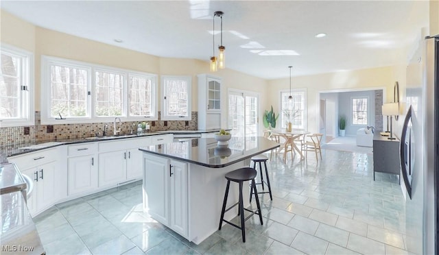 kitchen with dark countertops, backsplash, a breakfast bar, freestanding refrigerator, and a sink