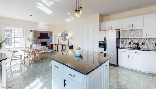 kitchen featuring tasteful backsplash, a kitchen island, dark stone countertops, a fireplace, and stainless steel refrigerator with ice dispenser