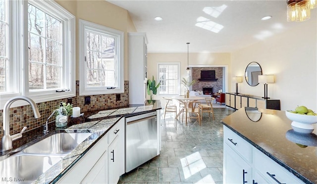 kitchen featuring stainless steel dishwasher, white cabinets, a fireplace, and a sink