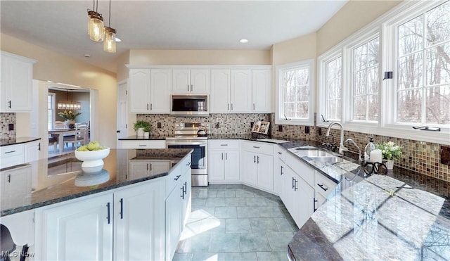 kitchen featuring dark stone countertops, a sink, appliances with stainless steel finishes, white cabinetry, and backsplash