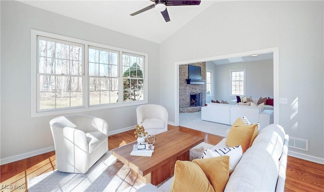 living area featuring visible vents, a brick fireplace, vaulted ceiling, wood finished floors, and a ceiling fan