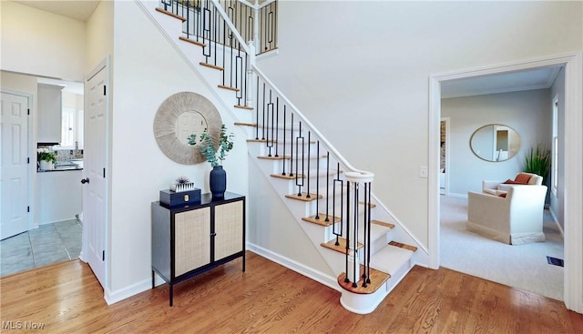 staircase with a high ceiling, baseboards, and wood finished floors