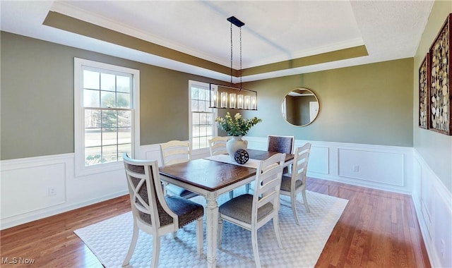 dining space with a notable chandelier, ornamental molding, a tray ceiling, wood finished floors, and wainscoting