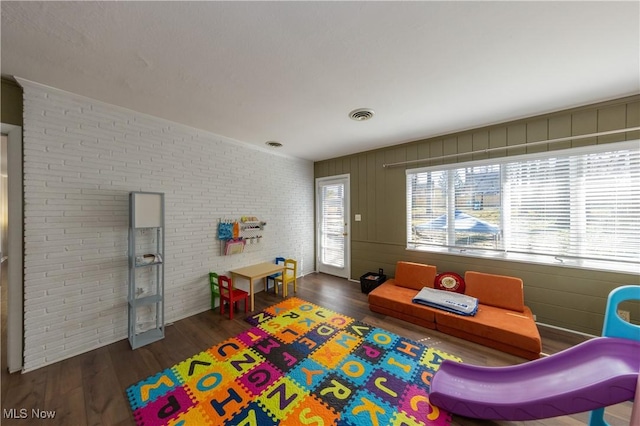 game room with visible vents, wood finished floors, and brick wall