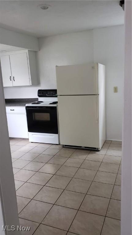 kitchen featuring light tile patterned floors, freestanding refrigerator, electric stove, white cabinetry, and dark countertops