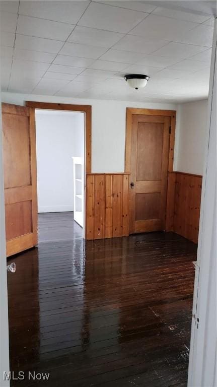 unfurnished room with wooden walls, wainscoting, and dark wood-type flooring