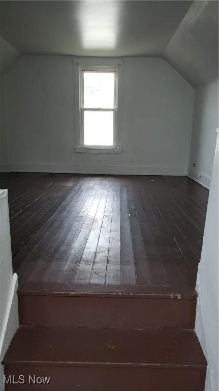 bonus room with lofted ceiling, dark wood-style floors, and baseboards