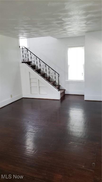 unfurnished living room featuring stairway, baseboards, and wood finished floors