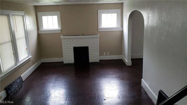 unfurnished living room featuring arched walkways, visible vents, plenty of natural light, and a brick fireplace