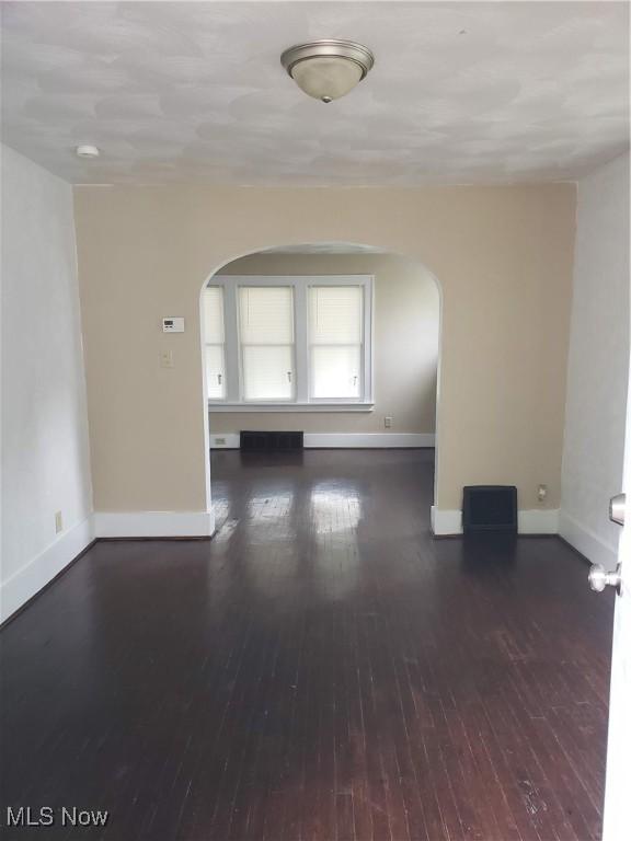 unfurnished room featuring hardwood / wood-style flooring, baseboards, and arched walkways