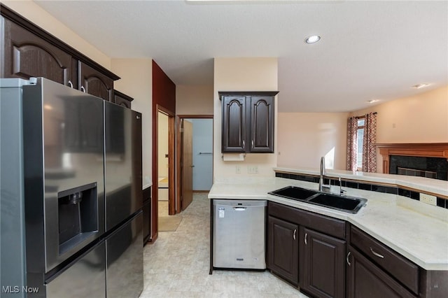 kitchen featuring a sink, a high end fireplace, dark brown cabinetry, appliances with stainless steel finishes, and light countertops