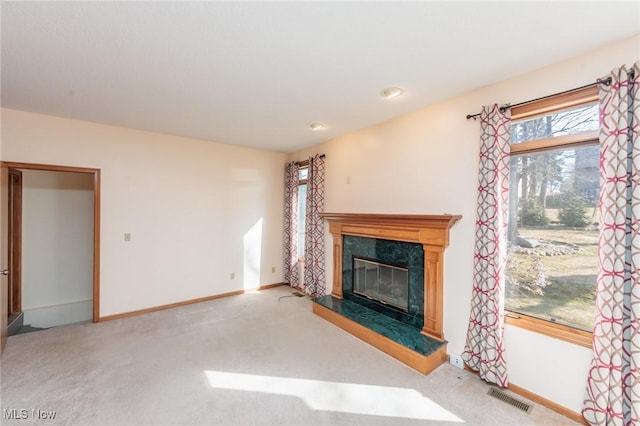 unfurnished living room with baseboards, visible vents, a high end fireplace, and light carpet