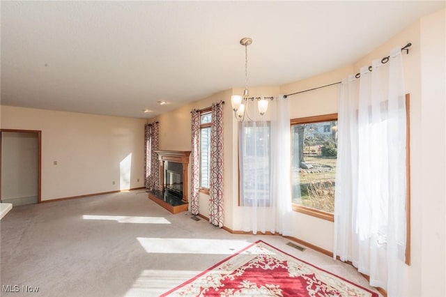 unfurnished living room with visible vents, carpet, baseboards, a chandelier, and a glass covered fireplace