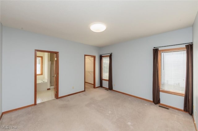 unfurnished bedroom with a spacious closet, visible vents, baseboards, light colored carpet, and a closet