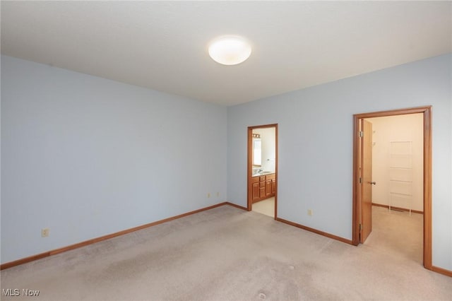 unfurnished bedroom with connected bathroom, baseboards, light colored carpet, and a spacious closet