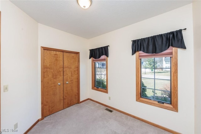 unfurnished bedroom featuring visible vents, multiple windows, light colored carpet, and baseboards