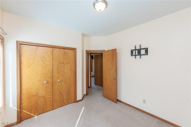 unfurnished bedroom with light colored carpet, a closet, and baseboards