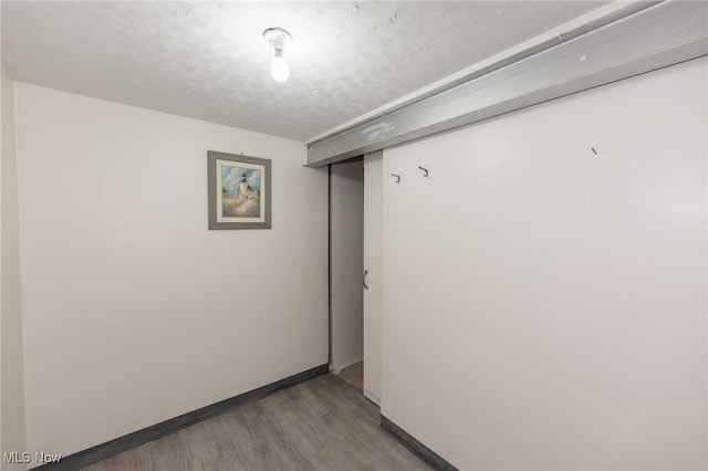 interior space with a textured ceiling, baseboards, and wood finished floors