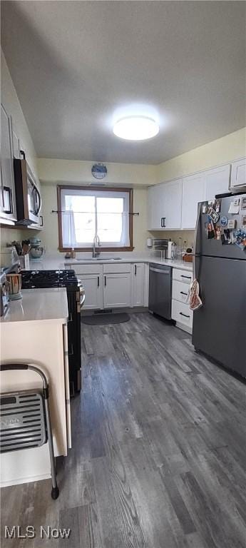 kitchen with dark wood finished floors, a sink, stainless steel appliances, light countertops, and white cabinets