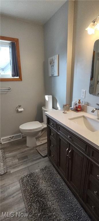 bathroom featuring vanity, wood finished floors, visible vents, baseboards, and toilet