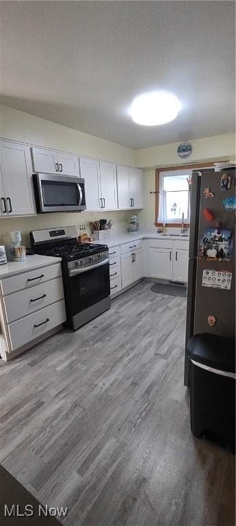 kitchen with white cabinets, stainless steel appliances, light wood-style flooring, and light countertops